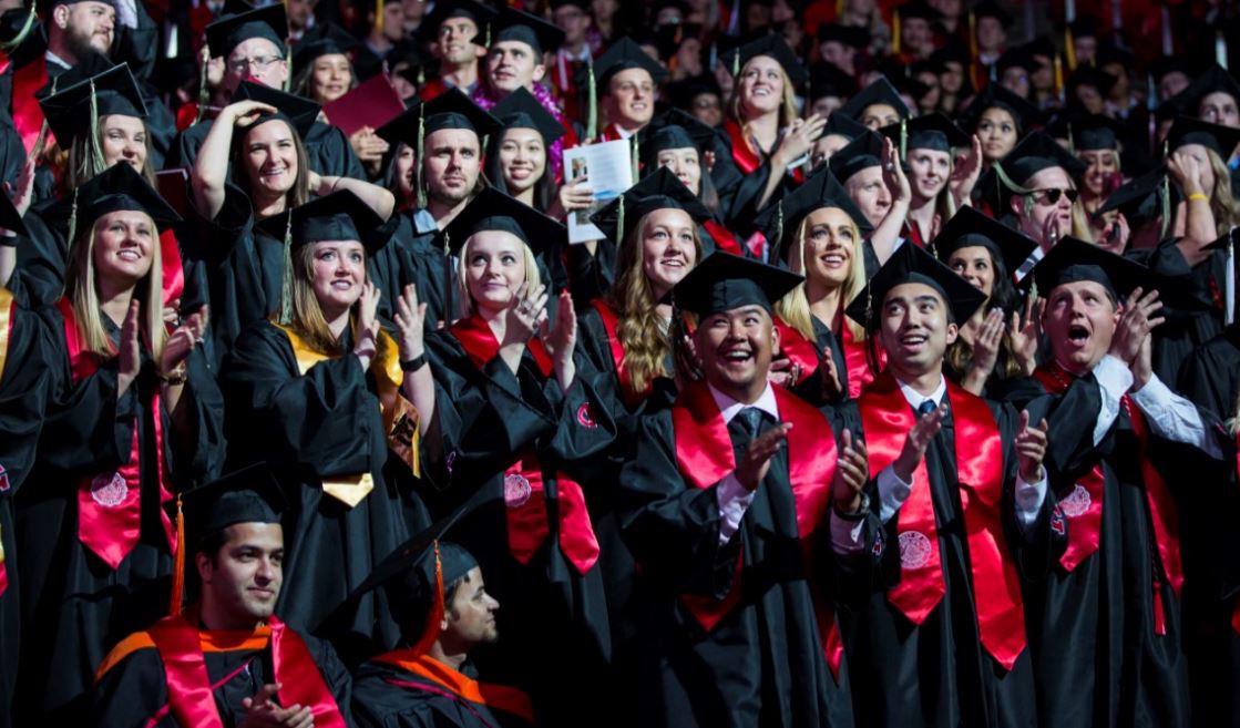 Group of students in caps and gowns at the commencement ceremony stand and cheer.