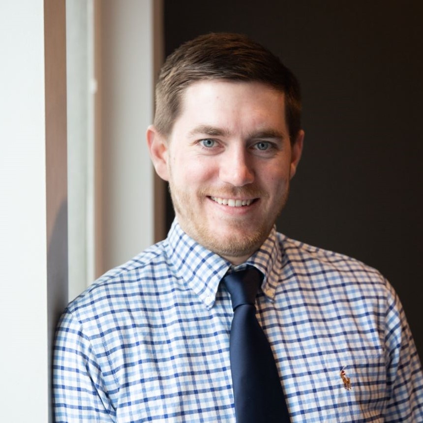 headshot of Jake Lemon, a white man with short brown hair wearing a plaid collared shirt and blue tie.